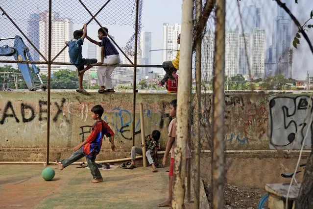 Boys play soccer as the city skyline is seen in the background in Jakarta, Indonesia, Friday, August 11, 2023. (Photo by Dita Alangkara/AP Photo)