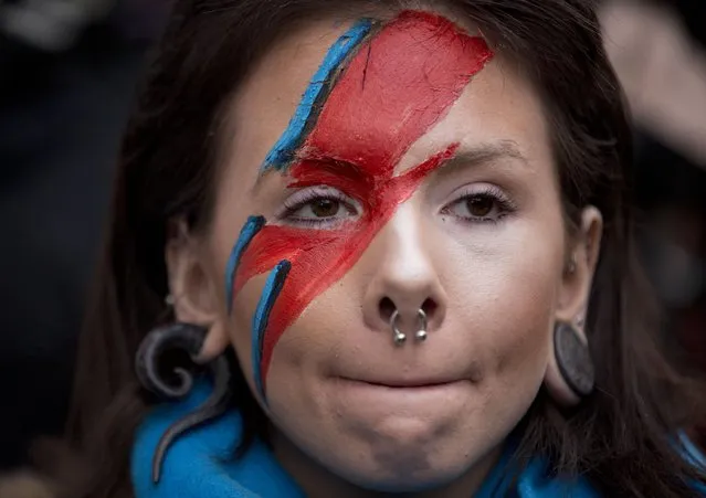 Fan Rosie Lowery wearing Bowie style make up talks to the media beside tributes placed next to a mural of British singer David Bowie by artist Jimmy C in Brixton, south London, Monday, January 11, 2016. Bowie, the other-worldly musician who broke pop and rock boundaries with his creative musicianship, nonconformity, striking visuals and a genre-spanning persona he christened Ziggy Stardust, died of cancer Sunday aged 69. He was born in Brixton. (Photo by Matt Dunham/AP Photo)