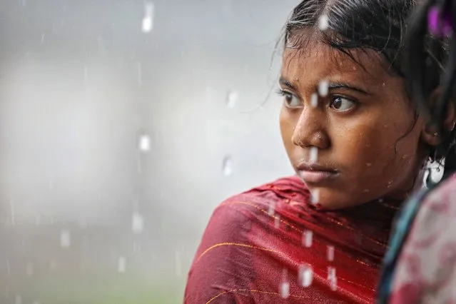 A girl looks on as she takes shelter under a shed during a downpour in Dhaka, Bangladesh on August 29, 2023. (Photo by Mohammad Ponir Hossain/Reuters)