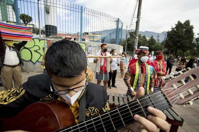 A musician plays a guitar and Tsachila Indigenous people stand together as they all wait outside the National Assembly for the start of the inauguration ceremony for President-elect Guillermo Lasso in Quito, Ecuador, Monday, May 24, 2021. (Photo by Carlos Noriega/AP Photo)