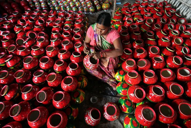 A woman decorates an earthen pitcher typically used during Garba, a folk dance, inside a workshop ahead of Navratri, a festival during which devotees worship the Hindu goddess Durga and youths dance in traditional costumes, in Ahmedabad, India October 3, 2018. (Photo by Amit Dave/Reuters)