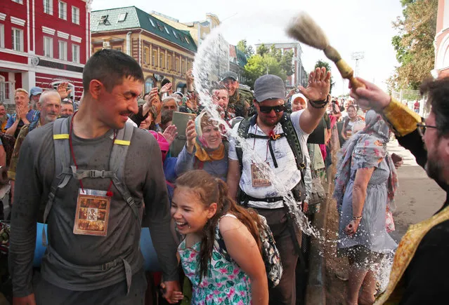 A Russian Orthodox priest sprinkles pilgrims with Holy Water during the Velikoretsky religious procession with a venerated wonderworking icon of St Nicholas in Kirov Region, Russia on June 8, 2021. The religious procession, one of the largest in Russia, is held annually from 3 to 8 June. The icon is believed to have been discovered by the Velikaya River in the 14th century. The 150 km route, which stretches from Kirov to the village of Velikoretskoye and back, attracts thousands of believers. (Photo by Dmitry Feoktistov/TASS)