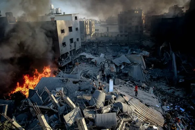 Smoke and fire rise from a levelled building as people gather amid the destruction in the aftermath of an Israeli strike on Gaza City on October 26, 2023, as battles continue between Israel and the Palestinian Hamas group. (Photo by Omar El-Qattaa/AFP Photo)