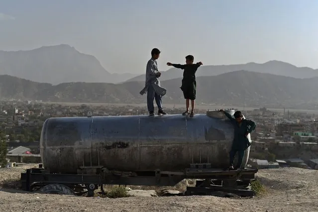 Afghan boys play on a water tanker at Nadir Khan hilltop overlooking Kabul on October 10, 2021. (Photo by Wakil Kohsar/AFP Photo)