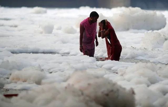 A Hindu couple worships the Sun god as they stand amidst the foam covering the polluted Yamuna river during the Hindu religious festival of Chhath Puja in New Delhi, India, November 10, 2021. (Photo by Adnan Abidi/Reuters)