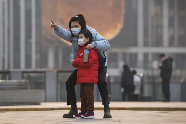 A woman and a child, both wearing face masks to protect from COVID-19 look at a commercial office building in Beijing, Sunday, November 28, 2021. (Photo by Andy Wong/AP Photo)