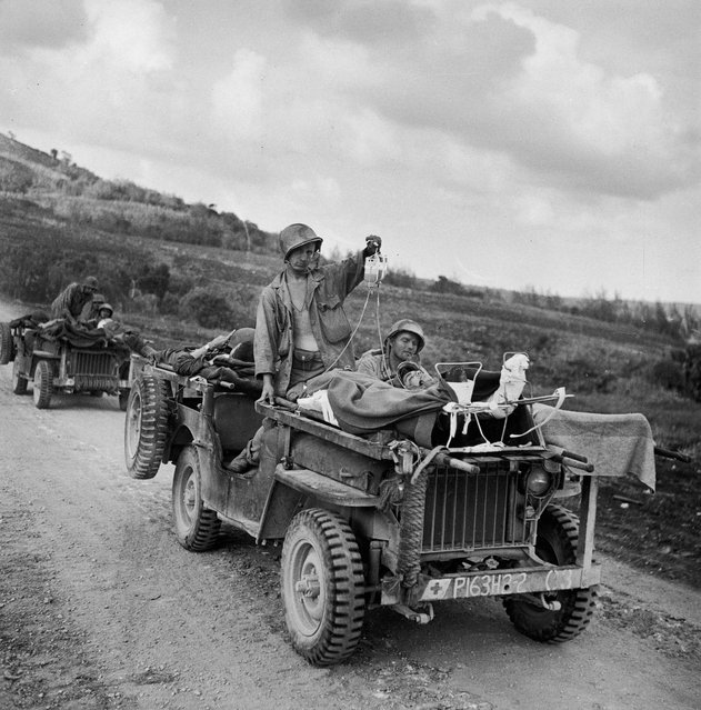 American soldiers drive the wounded away from the front lines during the fight to take Saipan, Northern Marianas Islands, June 1944. In the first jeep, one soldier drives while a second holds up IV bags attached to two injured men strapped to the vehicle's hood. (Photo by W. Eugene Smith/The LIFE Picture Collection/Getty Images)