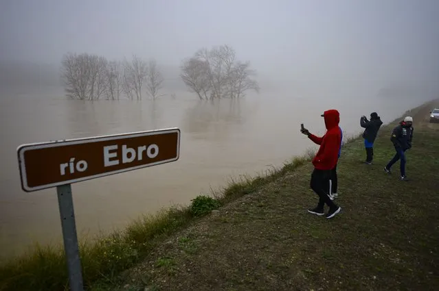 People stand beside the border of flooded area near the Ebro River in the small village of Pradilla de Ebro, Aragon province, northern Spain, Monday, December 13, 2021. Heavy rain has led to flooding in northern Spain. (Photo by Alvaro Barrientos/AP Photo)