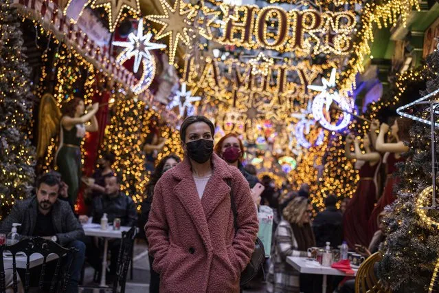 People wearing protective face masks walk outside a Christmas decorated coffee shop in Psiri district of Athens, on Monday, December 27, 2021. Part of new restrictions includes a mask mandate for outdoors and all public areas as the Greek government is expected to announce new measures to contain the spread of the Omicron variant. (Photo by Petros Giannakouris/AP Photo)