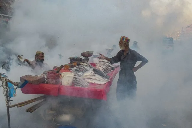 Vendors selling fish stand next to their cart duing a fumigation drive as a preventive measure against the diseases-carrying mosquitoes in Karachi on October 26, 2021. (Photo by Asif Hassan/AFP Photo)