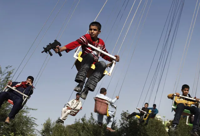 In this Sunday, September 20, 2009 file photo, an Afghan boy holds a toy gun as he enjoys a ride with others on a merry-go-round to celebrate the Eid al-Fitr festival, in Kabul, Afghanistan. (Photo by Anja Niedringhaus/AP Photo)