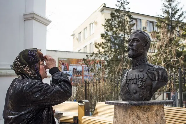 A woman prays at a bust of the last Russian Czar Nicholas II placed near the Crimean prosecutor's office, foreground, in Simferopol, Crimea, Monday, March 6, 2017. Russian news reports say curious and pious people are visiting a bust of the last Czar in the Crimean capital after reports spread that the sculpture appeared to be weeping. (Photo by Anton Volk/AP Photo)
