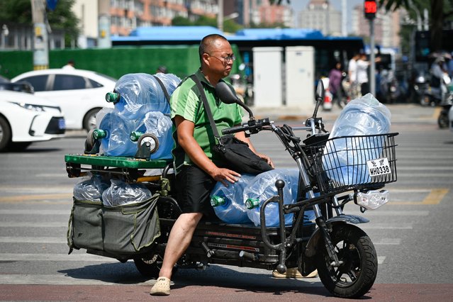 A man riding an electric delivery bike with water bottles waits to cross a street on a hot day in Beijing on June 18, 2024. (Photo by Wang Zhao/AFP Photo)
