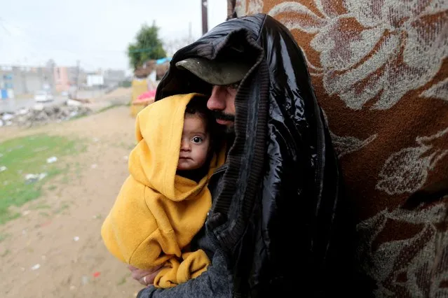 A Palestinian man stands outside with a child on a rainy day in Khan Younis, southern Gaza Strip on January 16, 2022. (Photo by Ibraheem Abu Mustafa/Reuters)