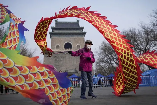 A resident wearing a face mask to help protect from the coronavirus twirls a dragon shaped ribbon near a barricaded coronavirus testing site setup outside the Drum Tower, Wednesday, March 23, 2022, in Beijing, China. A fast-spreading variant known as “stealth omicron” is testing China's zero-tolerance strategy, which had kept the virus at bay since the deadly initial outbreak in the city of Wuhan in early 2020. (Photo by Andy Wong/AP Photo)