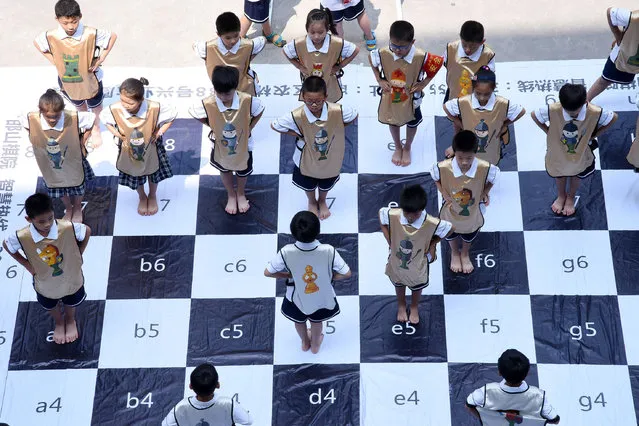 Children play chess on a giant chess board at a primary school in Handan in China's northern Hebei province on June 19, 2017. The “live” chess game was played by 32 students to promote chess at the school. (Photo by AFP Photo/Stringer)