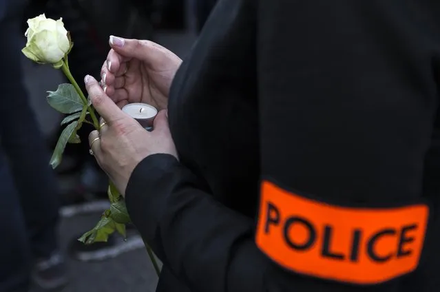 A French police officer holds a rose and an candle to pay homage to the two slain colleagues during a white march in Mantes-la-Jolie, west of Paris, Thursday, June 16, 2016. French police officials Jean-Baptiste Salvaing and his companion Jessica Schneider were killed Monday by an Islamic State extremist. (Photo by Kamil Zihnioglu/AP Photo)
