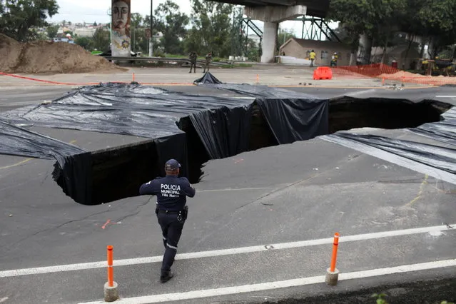 A municipal police officer walks near a sinkhole in a street caused by heavy rains in Villa Nueva, Guatemala on June 19, 2022. (Photo by Sandra Sebastian/Reuters)