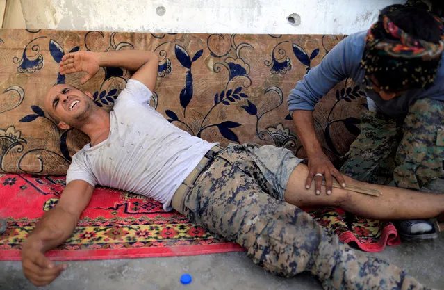 A member of the Syrian Democratic Forces who broke his leg during the fighting with Islamic State's fighters reacts while being bandaged by his comrade in the old city of Raqqa, Syria August 19, 2017. (Photo by Zohra Bensemra/Reuters)