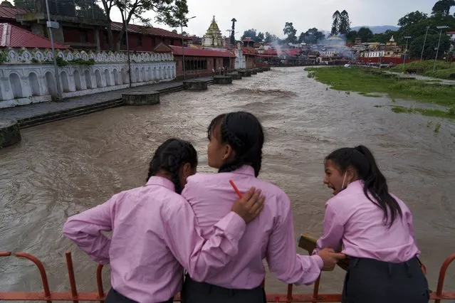Girls look at the Bagmati River, swelled by monsoon rains, in Kathmandu, Nepal, Wednesday, July 27, 2022. A governmental committee set up to help clean the river is working on upstream dams where rainwater can be captured and stored during the monsoon season and released during the dry months to flush the river, moving waste downstream from Kathmandu. (Photo by Niranjan Shrestha/AP Photo)