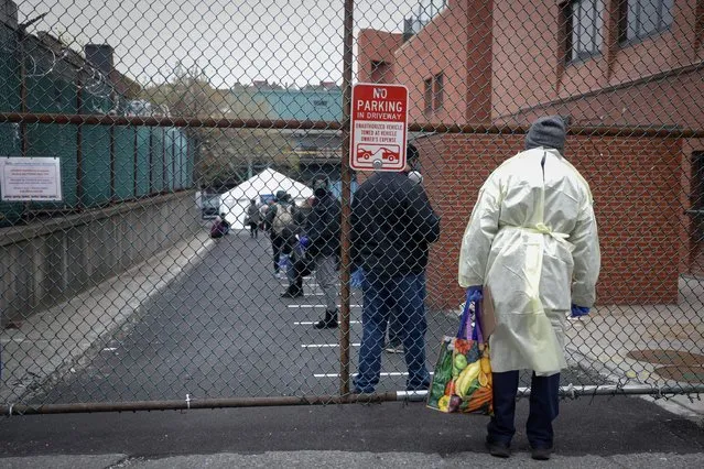 A healthcare worker looks through a fence at people waiting in line outside NYC Health + Hospitals/Gotham Health Morrisania neighborhood health center, one of New York City's new walk-in COVID-19 testing centers, during the outbreak of the coronavirus disease (COVID-19) in the Bronx borough of New York City, New York, U.S., April 20, 2020. (Photo by Mike Segar/Reuters)