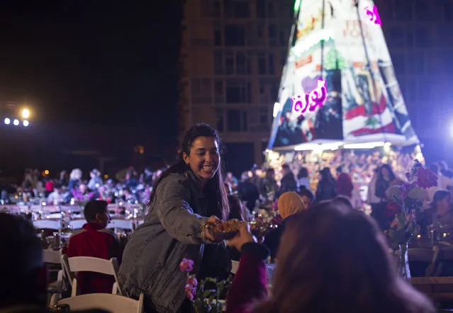 In this Monday, December 23, 2019, photo, a volunteer serves food at a public Christmas dinner, as an initiative to help those in need, in Martyrs Square where anti-government activists are encamped in Beirut, Lebanon. Lebanon is entering its third month of protests, the economic pinch is hurting everyone, and the government is paralyzed. So people are resorting to what they've done in previous crises: They rely on each other, not the state. (Photo by Maya Alleruzzo/AP Photo)