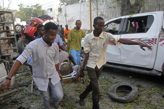 Somalis carry away the wounded civilian who was injured in a car bomb that was detonated in Mogadishu, Somalia Saturday, October 28, 2017. A suicide car bomb exploded outside a popular hotel in Somalia's capital on Saturday, killing at least 10 people and wounding more than 11, while gunfire could be heard inside, police said. A second blast was heard in the area minutes later. (Photo by Farah Abdi Warsameh/AP Photo)