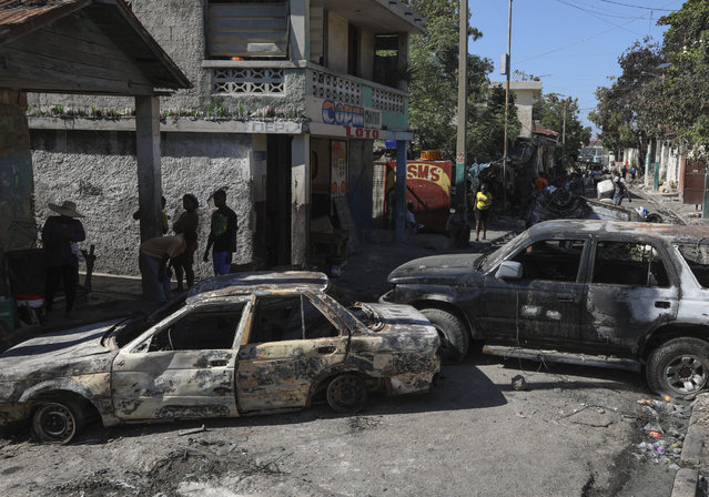 Residents walk past cars set on fire by armed gangs in the Poste Marchand neighborhood of Port-au-Prince, Haiti, Tuesday, December 10, 2024. (Photo by Odelyn Joseph/AP Photo)