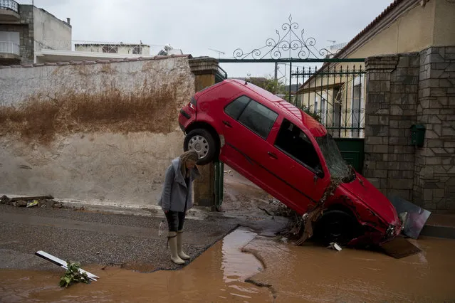 A woman stands in front of a washed up car at the entrance of a house in the municipality of Mandra western Athens, on Wednesday, November 15, 2017. Flash floods in the Greek capital's western outskirts Wednesday turned roads into raging torrents of mud and debris, killing at least nine people, inundating homes and businesses and knocking out a section of a highway. (Photo by Petros Giannakouris/AP Photo)