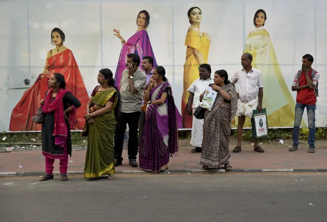 Indians returning after the day's work await bus transport standing on a pavement next to an advertisement hoarding of a clothing store in Thiruvananthapuram, Kerala state, India, Monday, December 18, 2017. Buses are an important means of public transport in India. (Photo by R.S. Iyer/AP Photo)