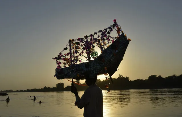 In this photograph taken on September 10, 2015, a Pakistani devotee carries a symbolic paper boat, an offering to Muslim saint Abdulqadir Jilani, as a way of giving thanks after their desire to give birth to a son was fulfilled before dropping it into the water during an annual ceremony on the banks of the River Ravi in Lahore. (Photo by Arif Ali/AFP Photo)