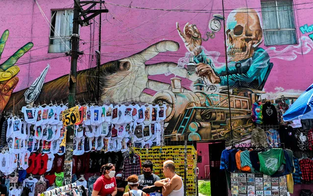 People wear face masks next to products displayed for sale in front of a wall depicting a mural at El Chopo flea market in Mexico City, on July 25, 2020, amid the novel coronavirus pandemic. (Photo by Pedro Pardo/AFP Photo)