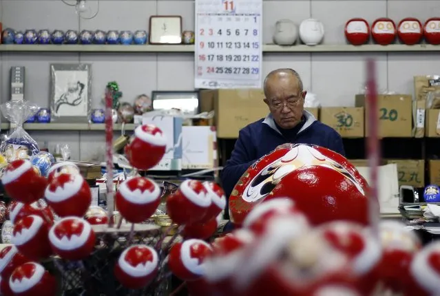Japanese craftsman Sumikazu Nakata adds the final touches on a Daruma doll, which is believed to bring good luck, in front of a calendar of November on a wall at his studio “Daimonya” in Takasaki, northwest of Tokyo November 23, 2014. (Photo by Yuya Shino/Reuters)
