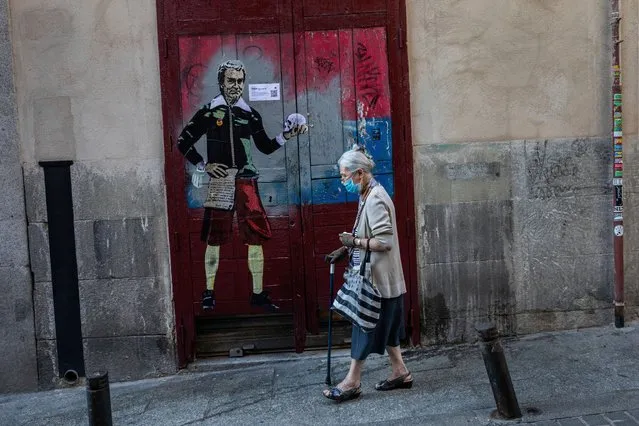 An elderly woman wearing a face mask to protect against the coronavirus walks past a painting named “to be or not to be” by artist TVBOY and depicting Spanish government's top virus expert Fernando Simon in Madrid, Spain, Sunday, September 13, 2020. (Photo by Bernat Armangue/AP Photo)