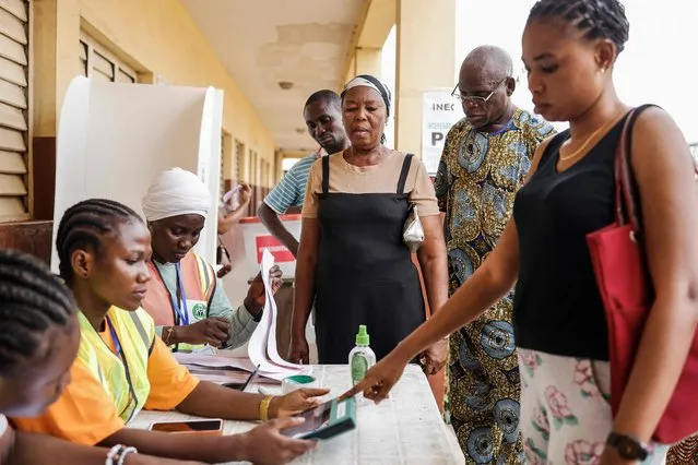 A voter looks on as another gets her information checked in the Bimodal Voter Accreditation System (BVAS) by an Independent National Electoral Commission (INEC) official at a polling station in Agege, Lagos, on February 25, 2023, during Nigeria's presidential and general election. (Photo by John Wessels/AFP Photo)