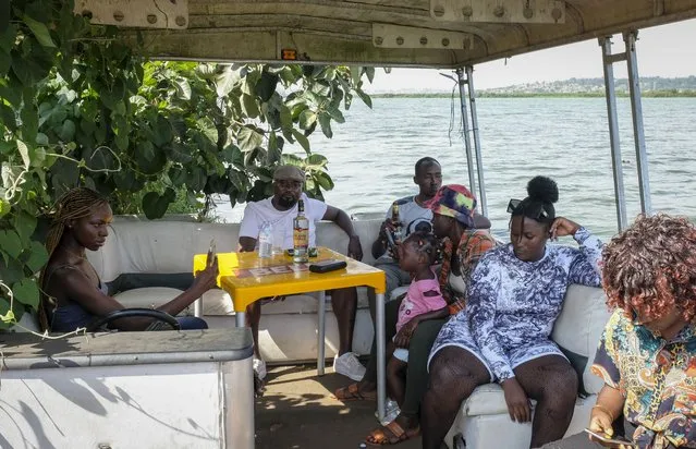People relax on a boat attached to a floating restaurant and bar, on Lake Victoria near the Luzira area of Kampala, Uganda Sunday, February 19, 2023. Flowering plants rise from the water into the wooden hull of James Kateeba's boat, used as a floating restaurant and bar that can be unmoored to drift for pleasure, but the greenery emerges from an innovative recycling project which uses thousands of dirt-encrusted plastic bottles to anchor the boat. (Photo by Hajarah Nalwadda/AP Photo)