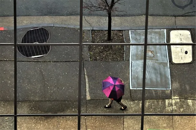 Reflected in the facade of the California State building in Santa Rosa, Calif., a pedestrian uses an umbrella to ward off the rain, Thursday, March 9, 2023. Evacuations were ordered Friday in Northern California after a new atmospheric river brought heavy rain, thunderstorms and strong winds, swelling rivers and creeks and flooding several major highways during the morning commute. (Photo by Kent Porter/The Press Democrat via AP Photo)