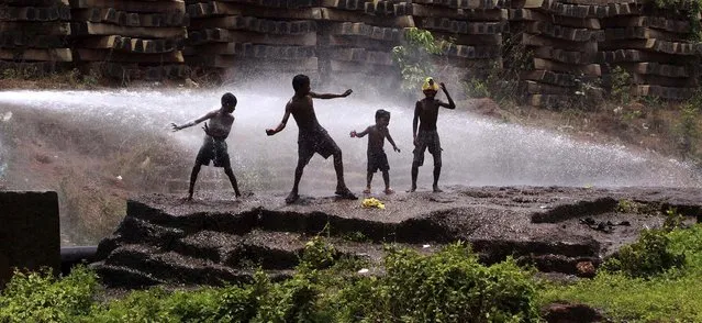 Children play in water sprinkling out of a water supply pipeline to beat the heat in Bhubaneswar, India, on May 21, 2013. (Photo by Biswaranjan Rout/Associated Press)