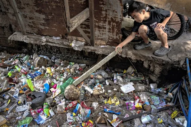A boy reaches for a ball on a creek clogged with plastic waste on April 15, 2023 in Caloocan, Metro Manila, Philippines. (Photo by Ezra Acayan/Getty Images)
