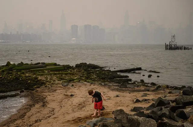 A child stands on the shore before the New York city skyline and east river shrouded in smoke, in Brooklyn on June 5, 2023. Smoke from the hundreds of wildfires blazing in eastern Canada has drifted south. Hundreds of wildfires were burning in Canada on June 6, 2023, according to the Canadian Interagency Forest Fire Centre, as fires have broken out across the country in recent weeks. Quebec alone had more than 150 active blazes across the province, the fire agency said. (Photo by Ed Jones/AFP Photo)