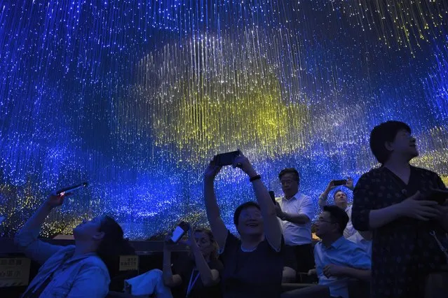 Passengers on a boat tour take photos of a light display underneath a bridge along an urban waterway in Beijing, Friday, June 30, 2023. (Photo by Mark Schiefelbein/AP Photo)