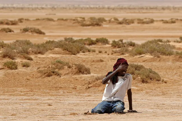A migrant of African origin collapses due to exhaustion and dehydration upon his arrival in an uninhabited area near al-Assah on the Libya-Tunisia border on July 30, 2023. (Photo by Mahmud Turkia/AFP Photo)