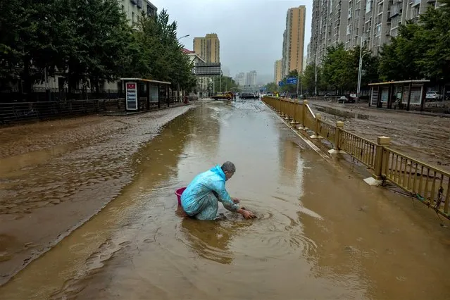 A man washes a cloth in a flooded street, in a neighbourhood where days of heavy rain from remnants of Typhoon Doksuri caused damage, in Beijing, China on August 1, 2023. (Photo by Thomas Peter/Reuters)