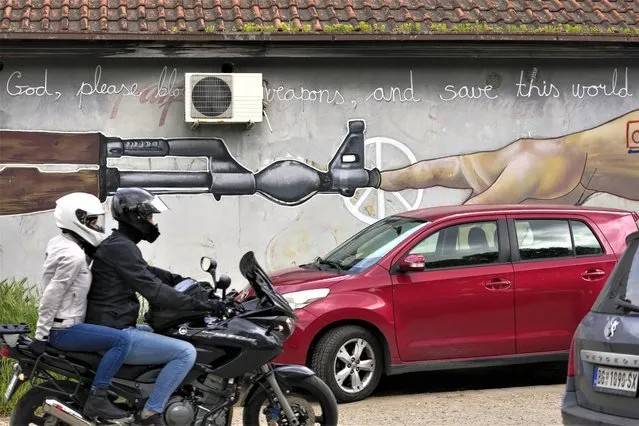 A man rides a motorcycle by a mural reading: “Good, please block the weapons and save this world” in Belgrade, Serbia, Tuesday, May 9, 2023. After two back-to-back mass killings that left 17 dead and 21 injured last week in Belgrade and two villages south of the capital, people were shocked. But many were not surprised in a country where war criminals are often glorified, where minority groups are harassed, where violence is openly displayed in the mainstream state-controlled media and where every second household has at least a gun stacked in a cupboard. (Photo by Darko Vojinovic/AP Photo)