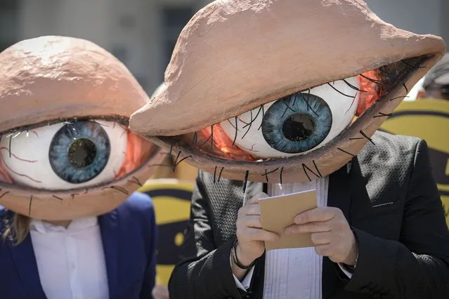 Activists wearing masks depicting large eyeballs attend a protest against planned updates of the country's national security laws, after a draft was leaked to the media earlier this month, in Bucharest, Romania, Wednesday, June 22, 2022. Dozens of activists gathered outside the government headquarters to protest against proposed changes to the laws that offer increased power to Romania's intelligence service (SRI), which include an obligation for citizens and companies to offer support to the service if requested. (Photo by Vadim Ghirda/AP Photo)