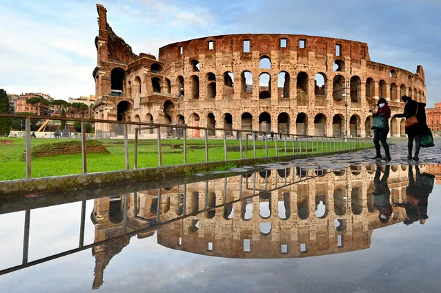 People walk past the Colosseum monument in Rome reflected in a pool of water on December 8, 2020 following heavy rains. (Photo by Alberto Pizzoli/AFP Photo)