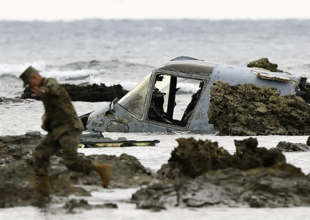 A member of the U.S. military personnel walks next to the wreckage of a U.S. Marine Corps MV-22 Osprey aircraft that crash-landed in the sea off Nago, in Nago, Okinawa Prefecture, Japan, in this photo taken by Kyodo December 14,  2016. (Photo by Reuters/Kyodo News)