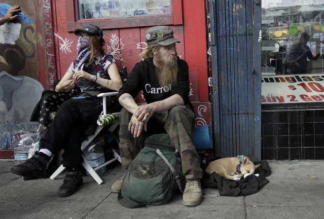 In this October 1, 2018 photo, Stormy Nichole Day, left, sits on a sidewalk on Haight Street with Nord (last name not given) and his dog Hobo while interviewed about being homeless in San Francisco. A measure on San Francisco's Nov. 6 ballot would levy an extra tax on hundreds of the city's wealthiest companies to raise $300 million for homelessness and mental health services. It's the latest battle between big business and social services advocates who say that companies such as Amazon, Google and Salesforce can afford to help solve severe inequities caused by business success. (Photo by Jeff Chiu/AP Photo)