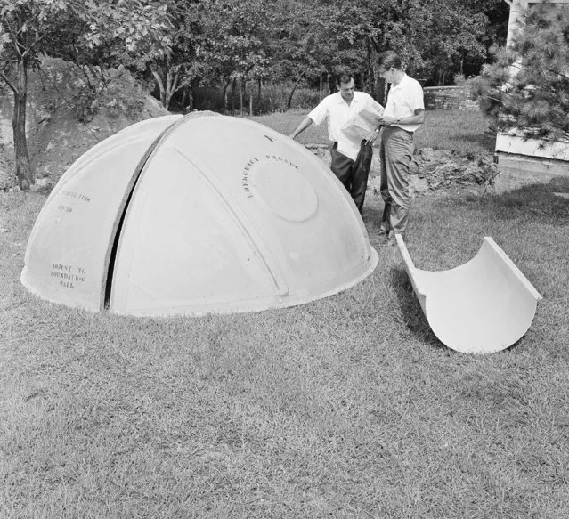 Engineers for a bomb shelter manufacturer, Vincent Carubia, left, and Eward Klein, study specifications for a fiber glass dome shelter being installed on an estate in Locust Valley, N.Y., on September 7, 1961. The dome is designed to cover an excavation, being dug in background, which is to be floored, walled and outfitted for emergency living. (Photo by AP Photo)