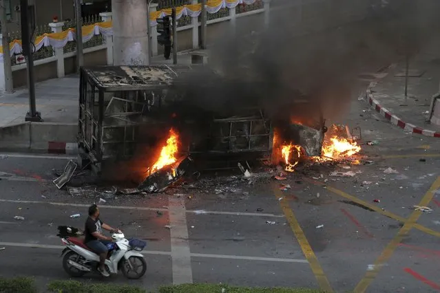A motorcycle ride pass the police detention truck was put on fire during a protest in Bangkok, Thailand, Saturday, August 7, 2021. Protesters demanded the resignation of Prime Minister Prayuth Chan-ocha and for part of the budget for the monarchy and the military to be redirected into the fight against the coronavirus. Many people blame Prayuth and his administration for failing to develop an adequate vaccination policy. (Photo by Nathathida Adireksarn/AP Photo)